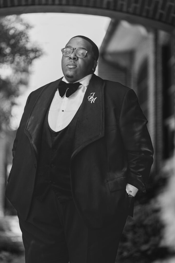 A black and white portrait of a person in formal attire wearing glasses and a tuxedo with a bowtie.