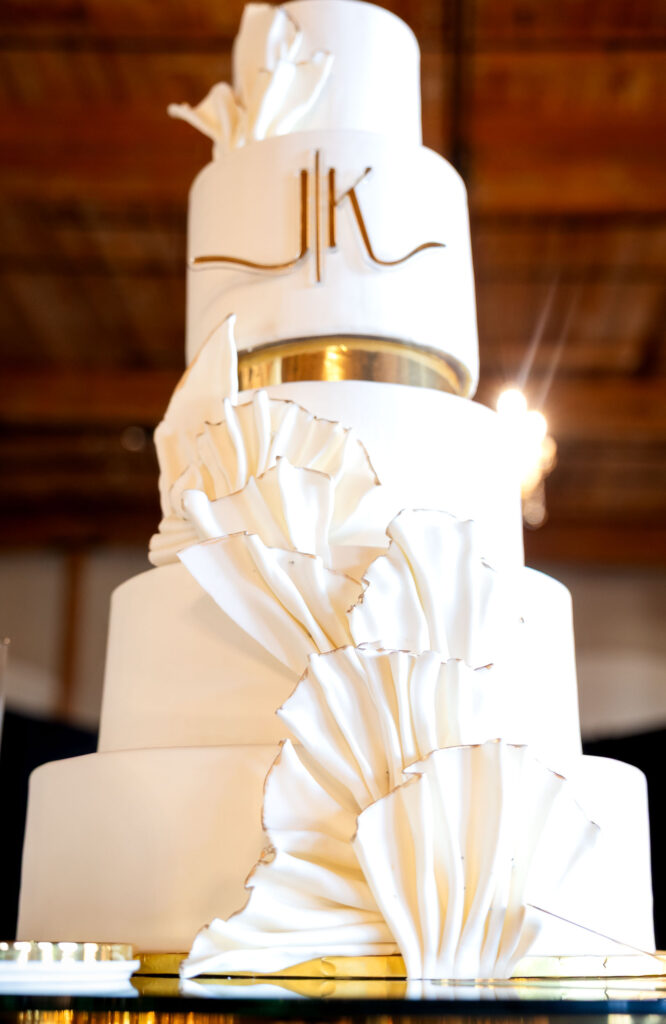 Modern white wedding cake decorated with geometric paper fan designs and metallic gold accents on each tier.