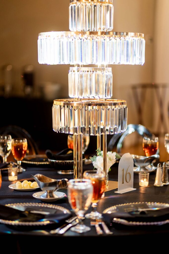 A tiered crystal centerpiece adorns an elegant black table setting with glowing candles and place settings at a formal event.